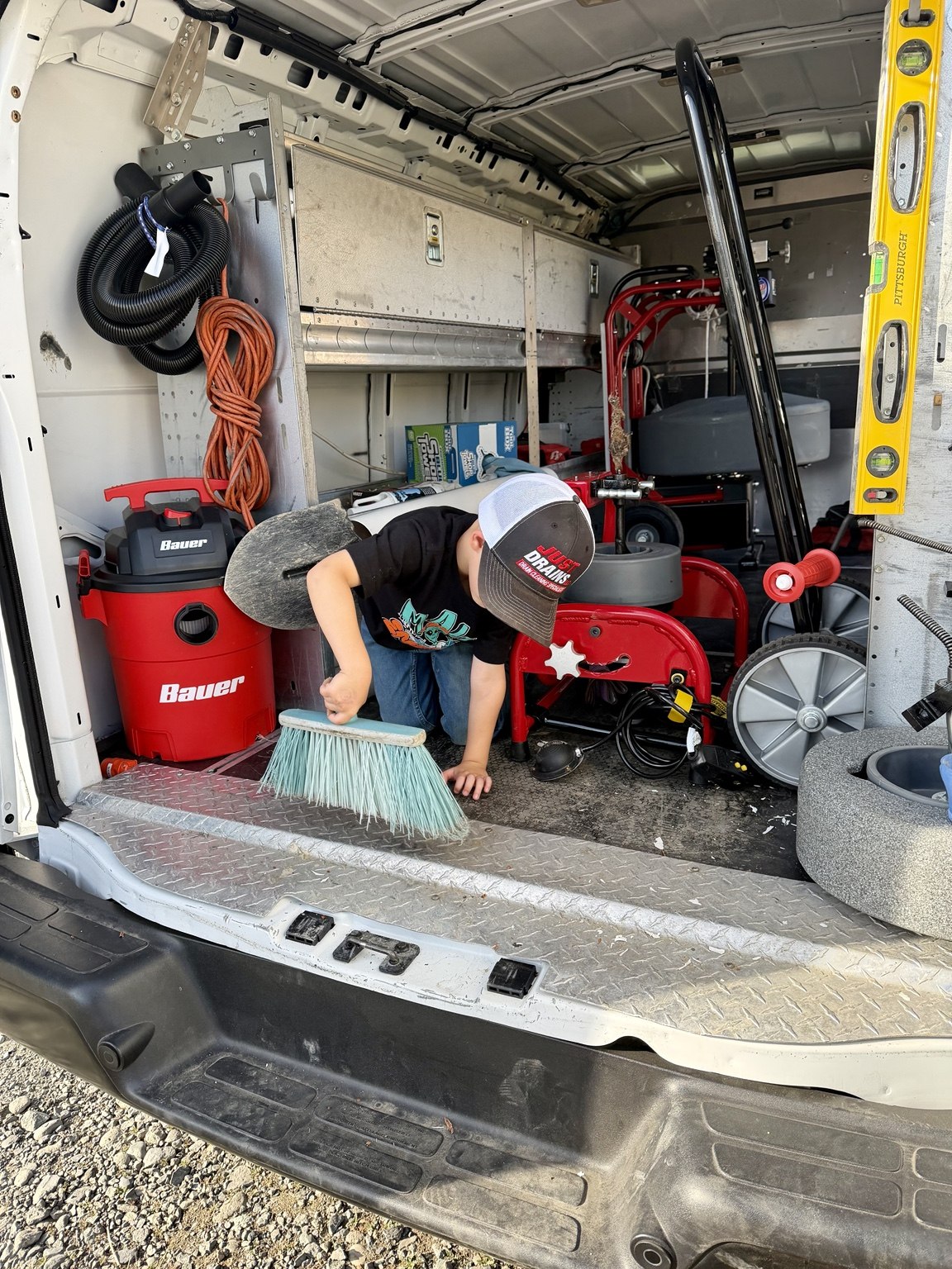 A young family helper sweeping the back of the Just Drains van